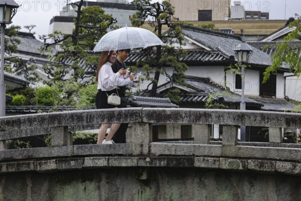 Two people with umbrellas on a bridge over a canal in traditional architecture, Kurashiki, Japan