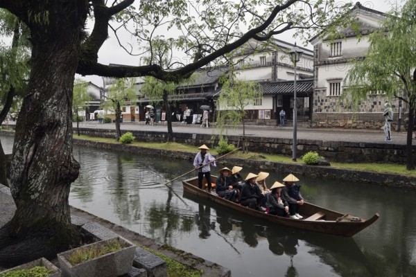 People in a traditional boat on a quiet canal surrounded by historic buildings, Kurashiki, Japan
