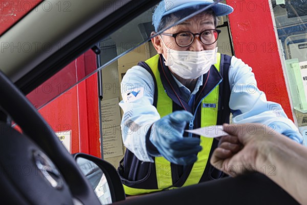 A cashier at a toll station exchanges papers with a motorist, Kobe, Hyogo, Japan