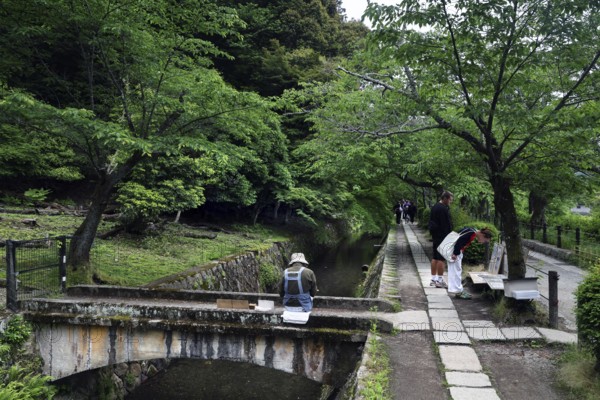 Painter on a Tetsugaku no Michi bridge surrounded by green nature and walkers, Kyoto, Okazaki, Japan