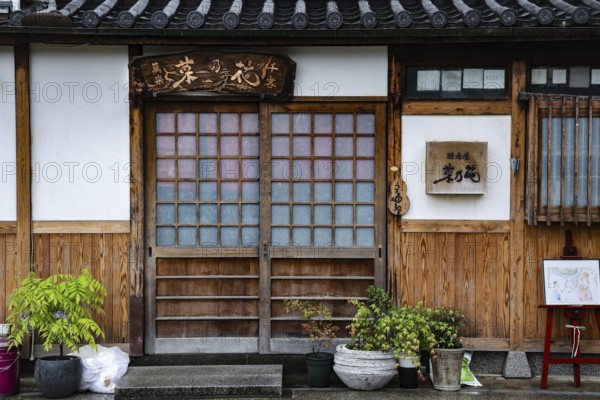 Entrance of a traditional Japanese building with decorated wooden door and potted plants, Kurashiki, Okayama, Japan