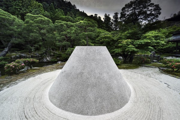 Zen garden with the cone-shaped sand hill Kogetsudai surrounded by green vegetation and trees, Kyoto, Japan