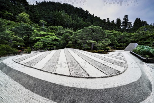 Zen garden of Ginkaku-ji Temple with precise sand patterns and rocks surrounded by green landscape, Kyoto, Japan