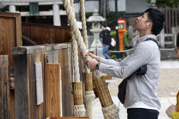 Man pulls a heavy rope to pray at a shrine, Kyoto, Higashiyama, Japan