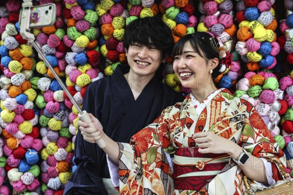Couple wearing kimonos taking selfies in front of colorful backgrounds at Yasaka Koshindo Temple, Kyoto, Higashiyama, Japan