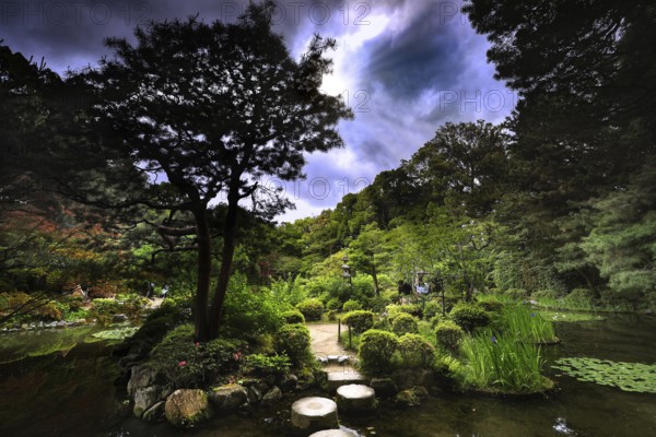 Stepping stones lead through the green garden under a dramatically cloudy sky, Kyoto, Okazaki, Japan