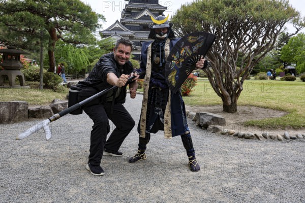 A samurai in traditional costume poses with a visitor in front of Matsumoto Castle, Matsumoto, Japan