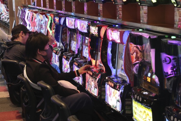 Men focus on glowing pachinko machines, Osaka, Japan