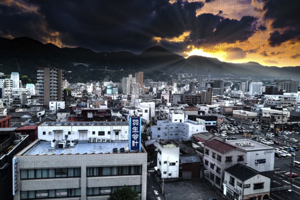 Dramatic city view of Beppu at sunset with mountains and dense buildings, Beppu, Japan