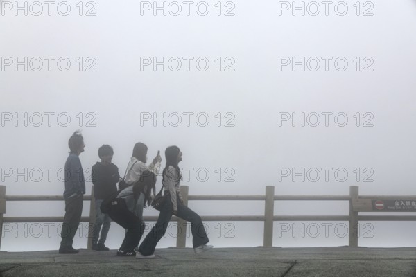 Tourists pose in front of fog-covered crater in Aso, Aso, Japan