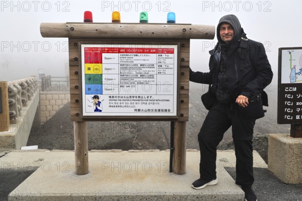 Person standing next to a warning sign in the fog of Nakadake Crater, Aso, Kumamoto, Japan