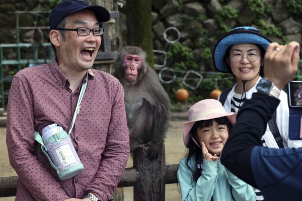 Visitors to Beppu pose for a photo with a Japanese macaque, Beppu, Oita, Japan