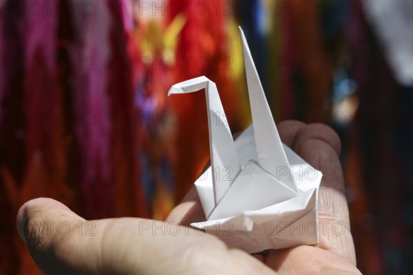 An origami crane is held by one hand in Hiroshima Peace Park, Hiroshima, Japan