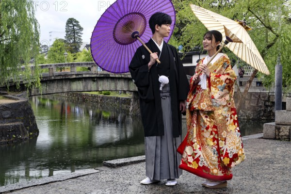 A traditionally dressed couple poses with umbrellas at a picturesque bridge, Himeji, Hyogo, Japan