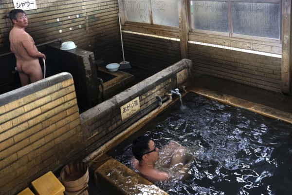 Traditional Japanese onsen bath with wooden walls in a warm setting. People enjoy the relaxing atmosphere, Beppu, Oita, Japan