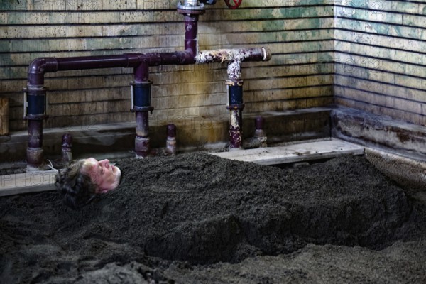 Person buried in sand in traditionally designed onsen area, Beppu, Takegawara Onsen, Japan