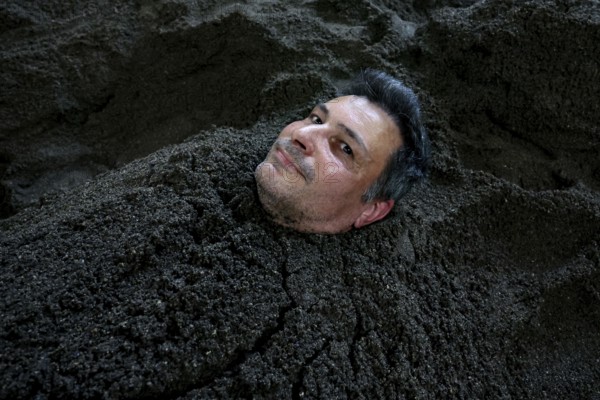 Man buried in sand bath with only his head sticking out, relaxed expression, Beppu, Takegawara Onsen, Japan