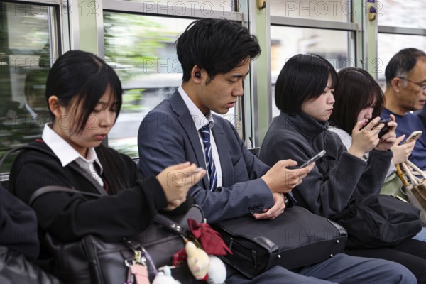 Passengers on a train in Kyoto, including a salaryman, use their smartphones, Arashiyama, Kyoto, Japan