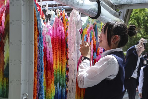 Schoolgirl arranges colorful paper cranes at the Peace Monument in Peace Park, Hiroshima, Japan