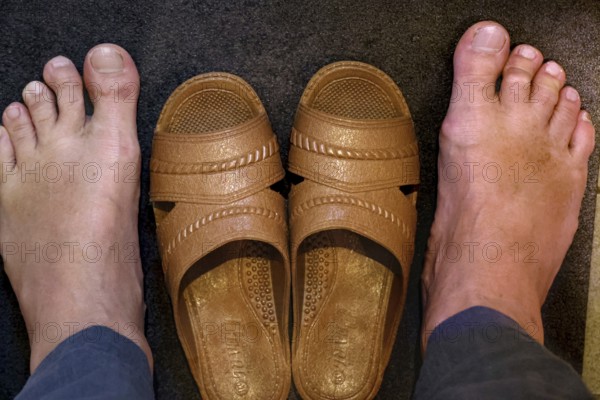 Two feet next to a pair of brown toilet shoes on dark ground, Osaka, zero, Japan