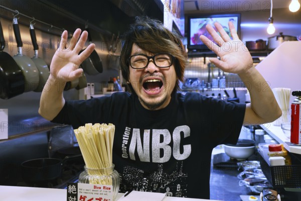 Man at ramen restaurant in Osaka greets with a smile and outstretched hands, Osaka, Japan