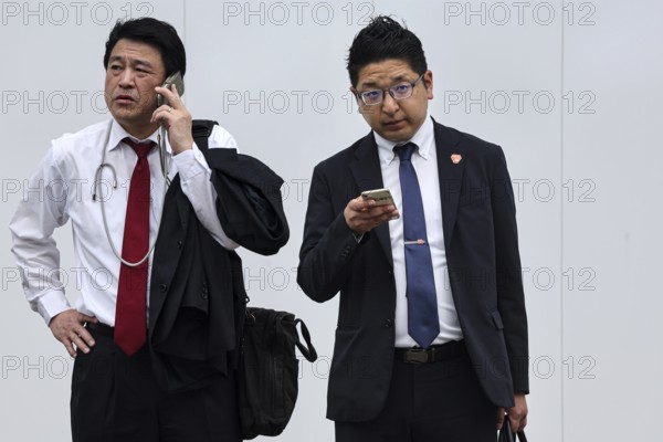 Two businessmen in suits, one talking on the phone, the other using a smartphone, Tokyo, Minato, Japan