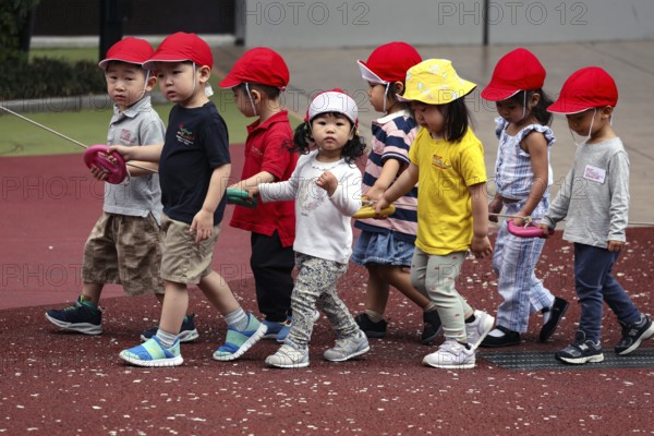 Kindergarten group wearing red caps walking on a playground, Tokyo, Minato, Japan