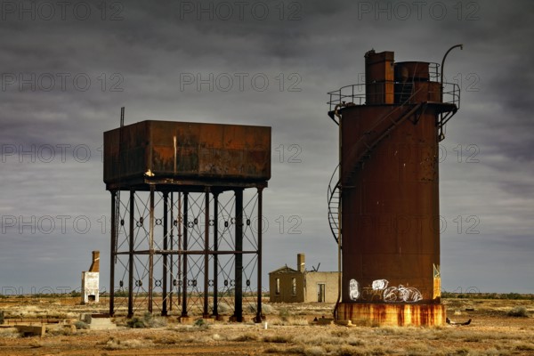 Rusty water towers and orphaned buildings under cloudy outback sky, Oodnadatta Track, null, Australia