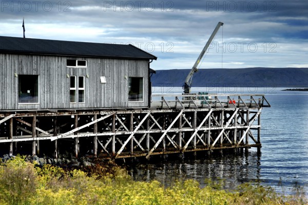 Wooden building on the water in Hamningberg under cloudy sky