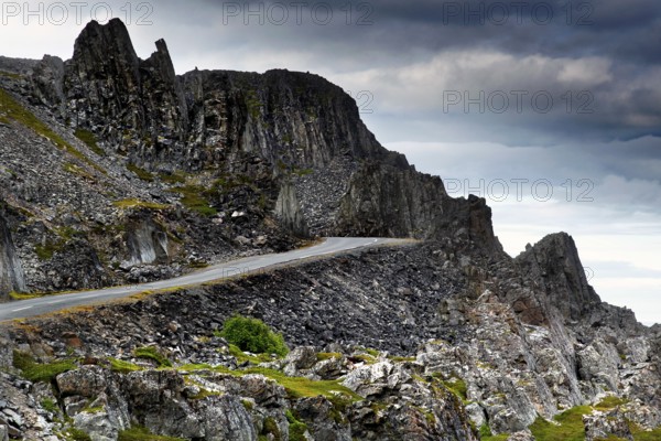 Coastal road nestles against rugged rocks under cloudy skies, N Hamningberg, zero