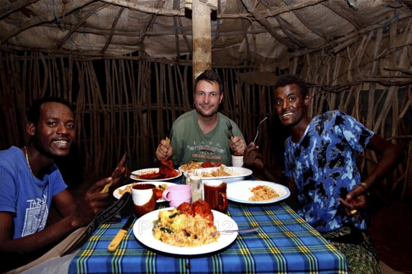 Three men enjoy a traditional dinner in a tent at camp in Ahmedela, Ahmedela, Ethiopia