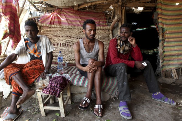 Three men sit relaxed in a café in Ahmedela surrounded by traditional decor, Ahmedela, Ethiopia