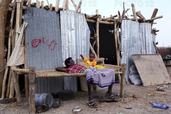A man and a child rest in front of a simple hut, Ahmedela, Tigray, Ethiopia