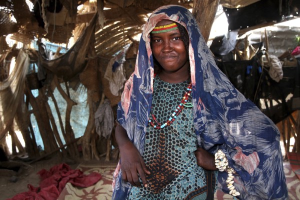 Aishe stands in Muhammad's hut wearing traditional clothes surrounded by coloured fabric in Ahmedela, Ahmedela, Ethiopia