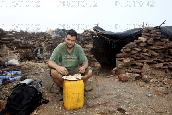 Man sitting in a warehouse of stone huts with minimalistic furniture, zero