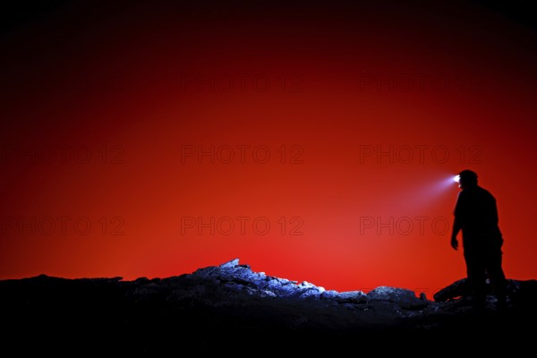 Silhouette of a human with head light against a bright red background, Erta Ale, Ethiopia