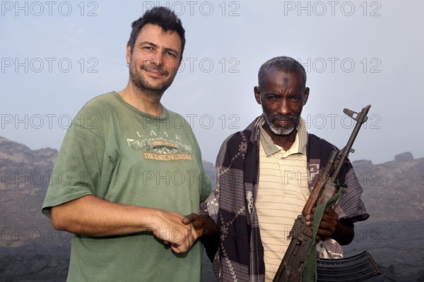 Police officer Muhammed stands next to a man in the volcanic landscape of Erta Ale, Erta Ale, Afar, Ethiopia