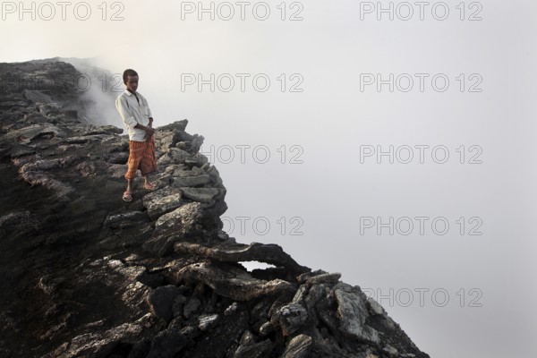 Mountain guide stands at the edge of a smoking crater in a foggy atmosphere, zero