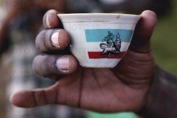 A hand holds a decorated cup during a coffee ceremony, Mayzebri, Ethiopia