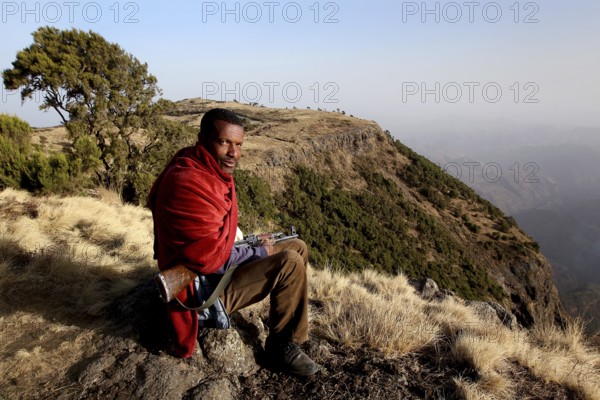 Armed companion sits in the impressive landscape of Semien Mountain National Park, Semien Mountain National Park, Ethiopia