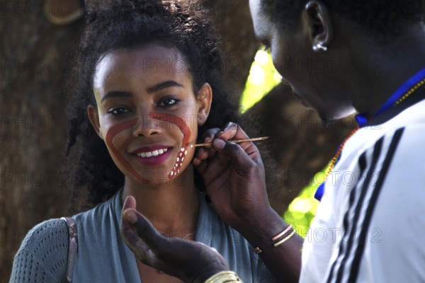 Tourist receives face painting from a hammer during an initiation ritual, outdoor cultural exchange, Turmi, null, Ethiopia