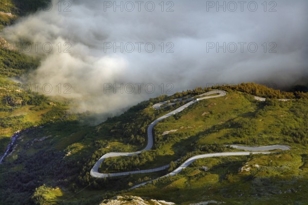 Serpentine road snakes through fog-covered green hills, Geirangerfjord, Dalsnibba, Norway