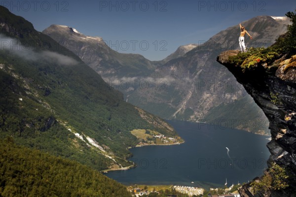 Adventurous tourist stands on cliff and enjoys views of Geirangerfjord, Flydalsjuvet, Geirangerfjord, Møre og Romsdal, Norway