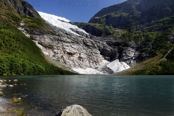 Bøyabreen Glacier Range stretches majestically against a blue sky, surrounded by steep mountains and crystal-clear water