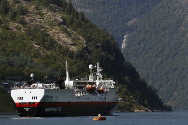A Hurtigruten ship on calm water off wooded mountain slopes, Geirangerfjord, Norway