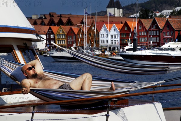 Man in a hammock on a boat with a view of the Tyskebryggen Hanseatic Quarter, Bergen, Norway