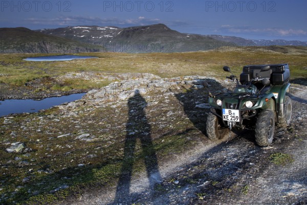 ATV is standing on a dirt road next to a long shadow of people in the vast countryside, zero