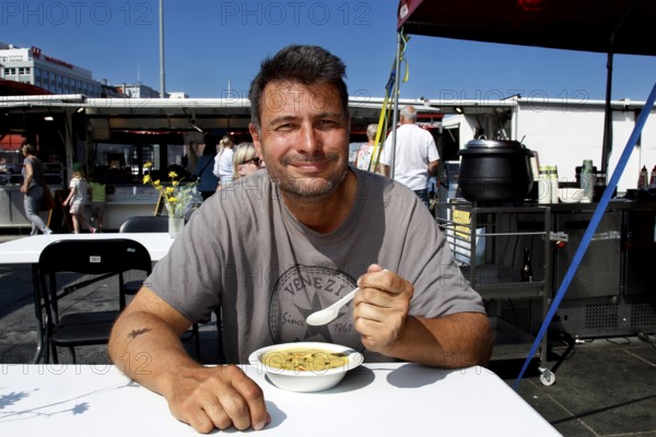 Smiling man eating at fish market in sunshine, Bergen, Hordaland, Norway