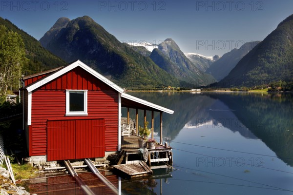 Idyllic red cabin on a quiet fjord with majestic mountains all around, Mundal, Norway