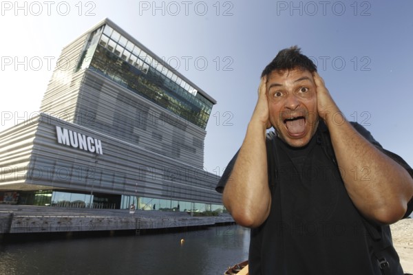 A man poses in front of the Munch Museum in a well-known screaming pose, Oslo, Bjøvika, Norway
